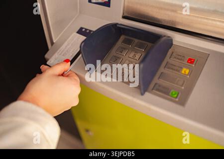 Hand inserting card into ATM for cash withdrawal in urban setting Stock Photo