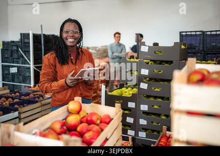 Woman checking fresh organic apples in warehouse using digital tablet Stock Photo