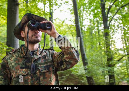 Soldier wearing camouflage uniform using binoculars in forest Stock Photo