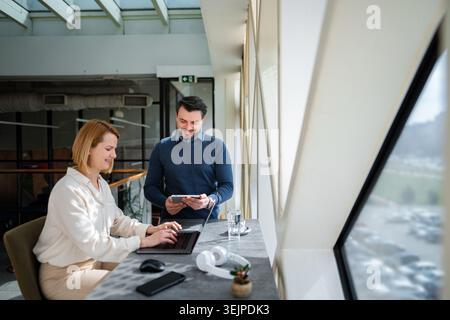 Business colleagues collaborating on devices, smiling and analyzing data in a sunny office Stock Photo