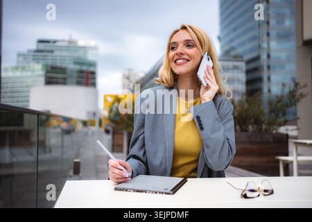 Young businesswoman talking on phone and using tablet outdoors Stock Photo