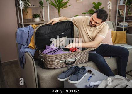 Smiling man packing suitcase for business trip at home Stock Photo