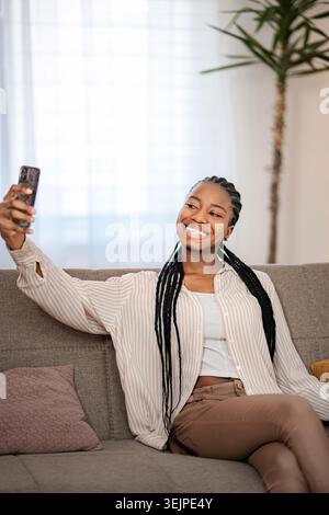 Young black woman taking selfie with smartphone on sofa Stock Photo
