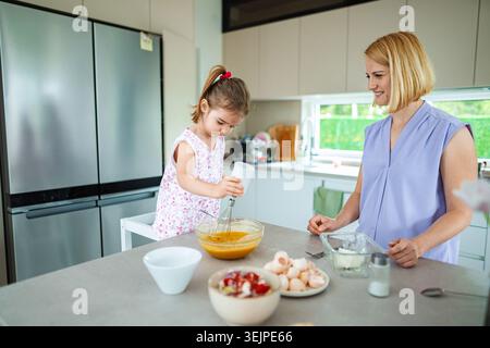 Mom and daughter baking together in a sunny kitchen Stock Photo