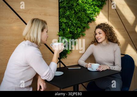 Two women friends having coffee and conversation in modern cafe Stock Photo