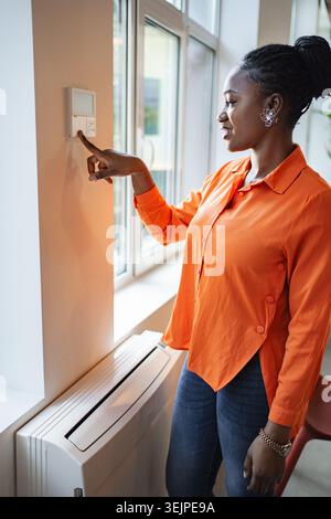 Woman in Orange Shirt Pointing at Light Switch Stock Photo