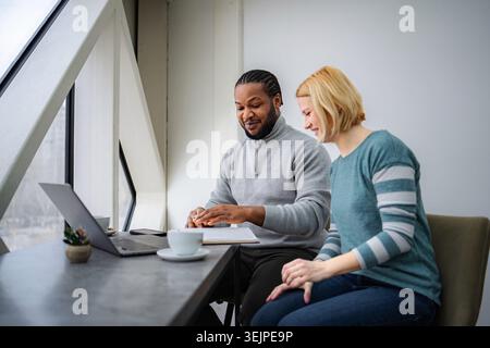 Two business partners collaborating on a laptop and notebook at a modern office Stock Photo