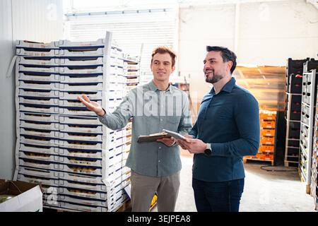 Two men collaborating on logistics and distribution in a large warehouse Stock Photo