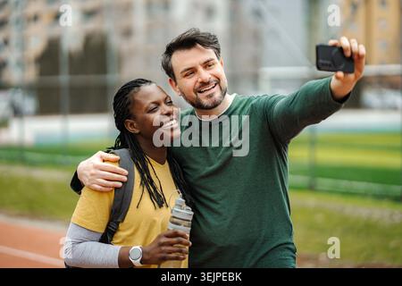 Diverse couple smiling, embracing, and taking selfie together with smartphone Stock Photo