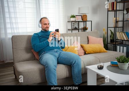 Man relaxing on sofa wearing headphones and using phone Stock Photo