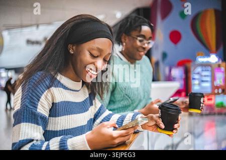 Happy young women using smartphones and drinking takeaway coffee Stock Photo