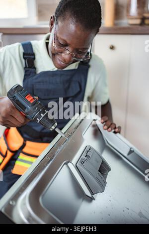 Technician repairing dishwasher using electric screwdriver in a kitchen Stock Photo