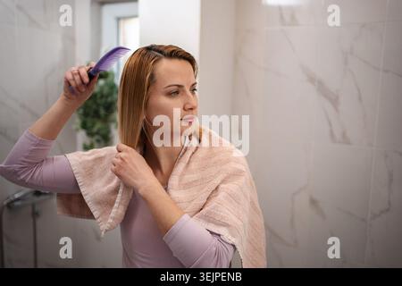 Young woman combing her hair after a shower, wearing a towel Stock Photo