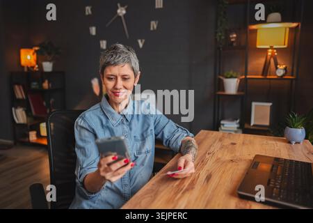 Woman making online payment using smartphone and credit card at home Stock Photo