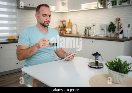Adult man drinking coffee and using tablet in kitchen Stock Photo