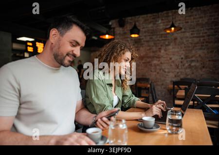 Young smiling couple using laptop and smartphone while drinking coffee in a cafe Stock Photo