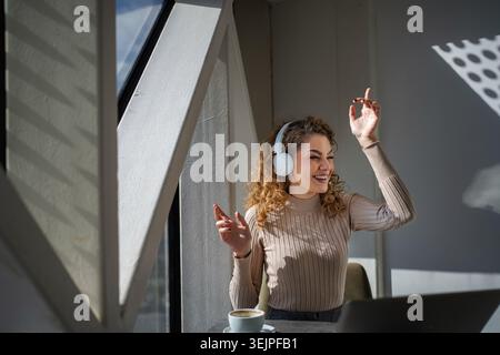 Young woman enjoying music with headphones remote working at cafe Stock Photo
