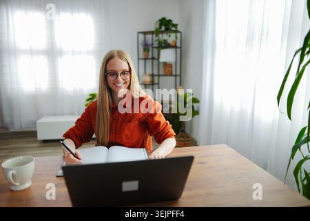 Woman writing in a notebook while sitting at a desk indoors Stock Photo