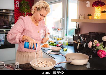 Woman seasoning sliced mushrooms in a pan on a stovetop Stock Photo