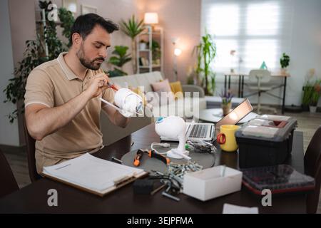 Security technician assembling modern wireless surveillance camera at home using instructions and laptop Stock Photo