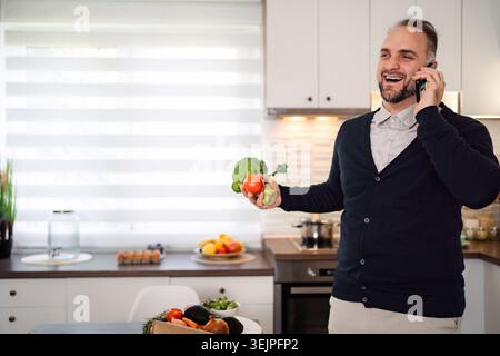 Man talking on phone holding vegetables in kitchen Stock Photo