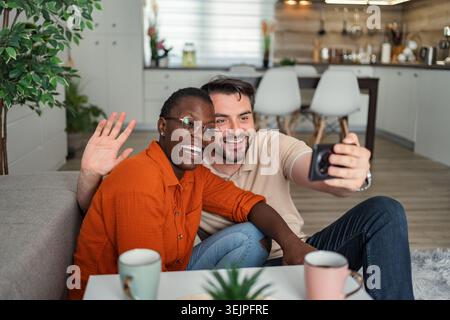 Happy multiethnic couple video calling with family using smartphone at home Stock Photo