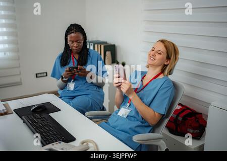 Nurses relaxing using cell phones during break laughing Stock Photo