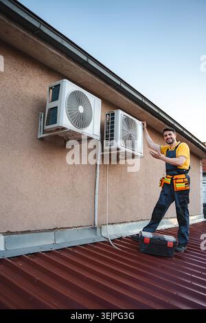 HVAC technician is installing an air conditioner on a building rooftop Stock Photo