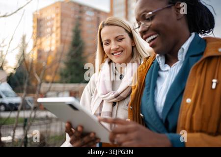 Diverse women colleagues collaborating on digital tablet outdoors Stock Photo