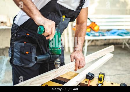 Unrecognizable male carpenter using electric drill on a wooden plank outdoors Stock Photo