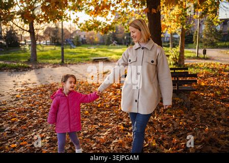 Mother and daughter holding hands walking in autumn park Stock Photo