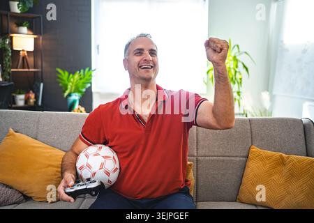 Excited middle aged man playing soccer video game at home Stock Photo