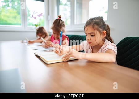 Children engaged in creative writing at a sunlit table Stock Photo