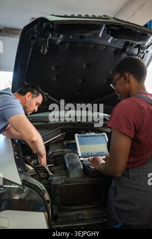 Mechanics repairing car engine using laptop in auto repair shop Stock Photo