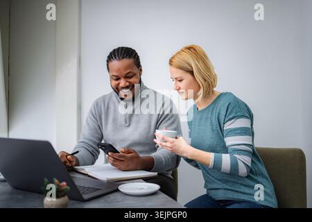 Diverse couple using smartphone and laptop for work Stock Photo