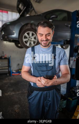Happy mechanic using mobile phone in a car repair shop Stock Photo