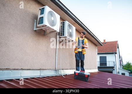 Technician installing air conditioning units using smartphone on a roof Stock Photo