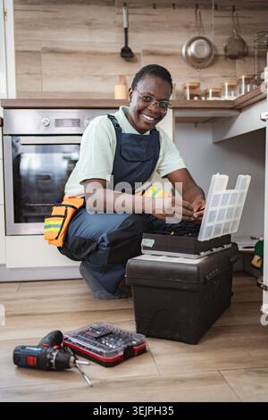 Smiling african american female plumber fixing pipes under kitchen sink Stock Photo