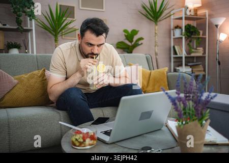 Freelancer drinking lemonade and working from home on laptop Stock Photo
