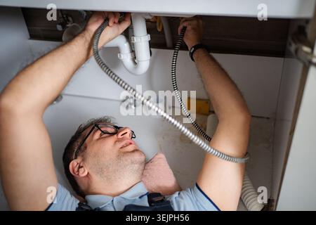 Plumber working on a sink pipe blockage in kitchen Stock Photo