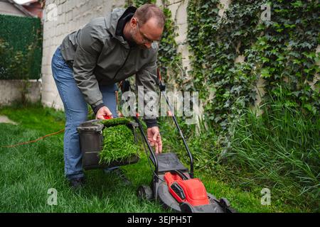 Man carefully trims grass in a lush garden as evening sunlight filters through green leaves Stock Photo