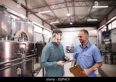 Brewery workers discussing production planning using digital tablet Stock Photo