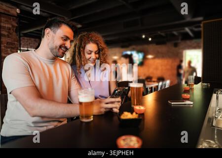 Couple enjoying drinks and using smartphone at bar counter Stock Photo