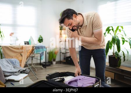 Man talking on the phone while packing his suitcase at home Stock Photo