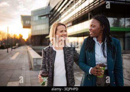 Two diverse businesswomen walking and talking during coffee break Stock Photo