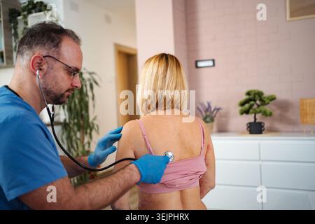 Doctor examining patient with stethoscope during home visit Stock Photo