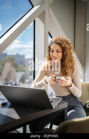 Young adult woman enjoying coffee working on laptop Stock Photo