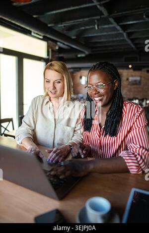 Diverse businesswomen collaborating on laptop during coffee break Stock Photo