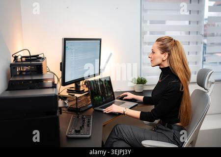 Young adult woman programming on laptop and monitor in modern home office Stock Photo