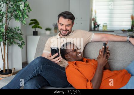 Interracial couple relaxing on sofa using smartphones at home Stock Photo